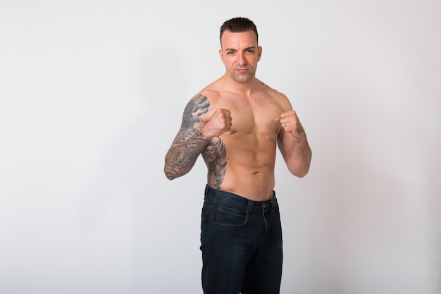 Portrait Of Shirtless Man With Tattoos Against White wall