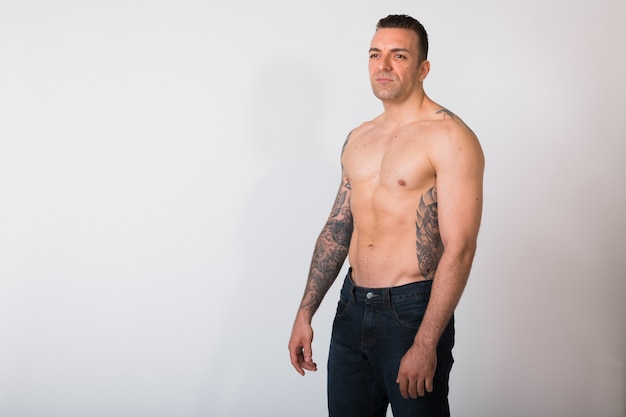 Portrait Of Shirtless Man With Tattoos Against White wall