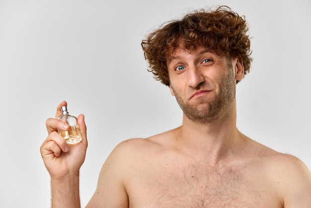 Portrait of shirtless mature man with curly hair applying perfume against grey studio background