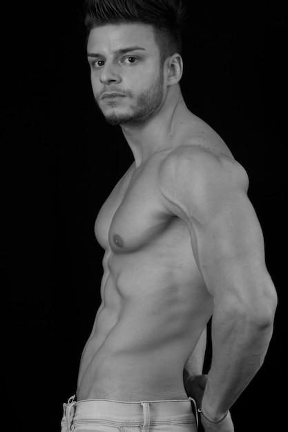 Photo portrait of shirtless muscular man standing against black background