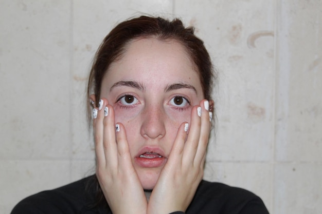 Photo portrait of shock young woman with hands on cheeks against wall