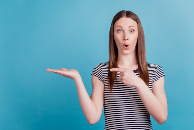 Portrait of shocked adviser girl indicate forefinger hand hold empty space open mouth on blue background