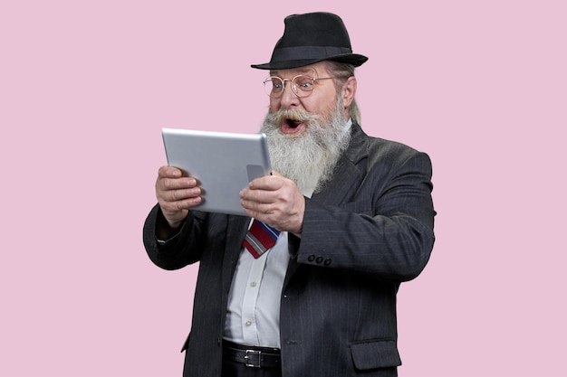 Portrait of shocked aged man with tablet pc Isolated on pink