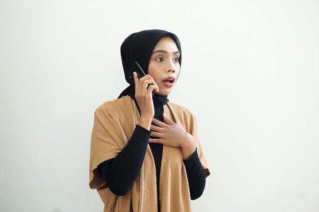 Портрет шокированной азиатской мусульманки в хиджабе, звонящей по мобильному телефону