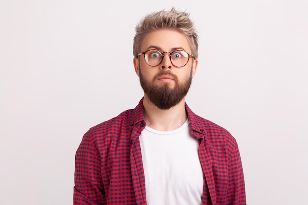 Portrait of shocked by news bearded man freelancer in eyeglasses and checkered shirt surprisingly looking at camera. Indoor studio shot isolated on gray background