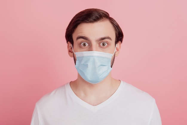 Portrait of shocked excited guy wear protective medical mask staring on pink background