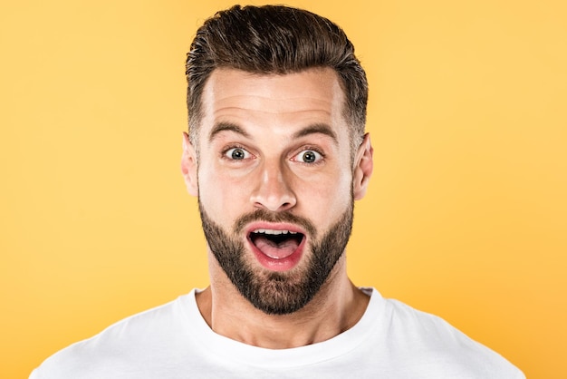 Portrait of shocked handsome man in white tshirt isolated on yellow