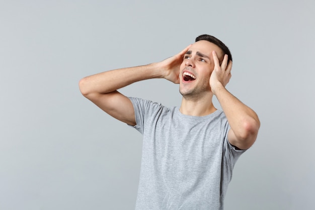 Portrait of shocked screaming young man in casual clothes looking aside, putting hands on head 