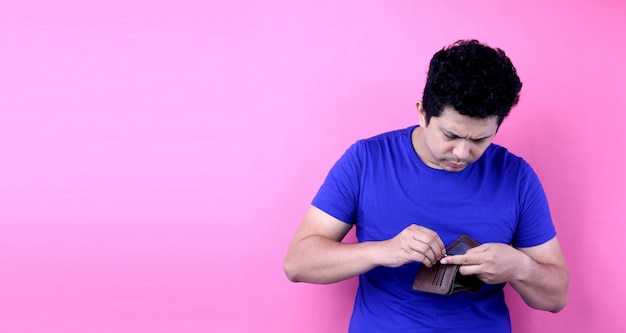 portrait of a shocked, surprised speechless man asia, holding an empty wallet on pink background in studio