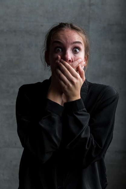 Portrait of shocked woman covering mouth with hands against wall
