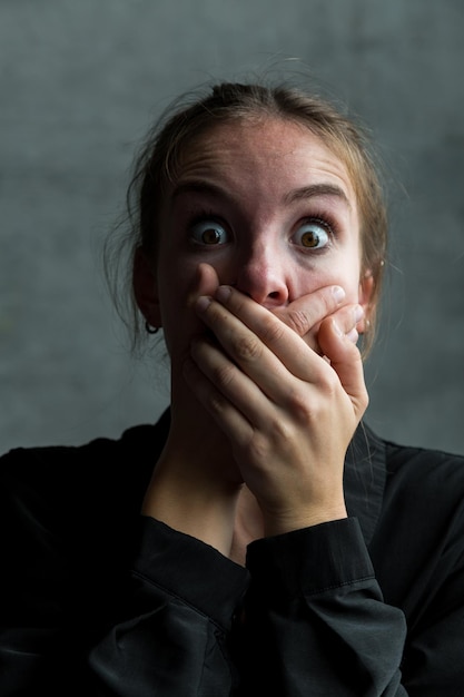 Portrait of shocked woman covering mouth with hands against wall