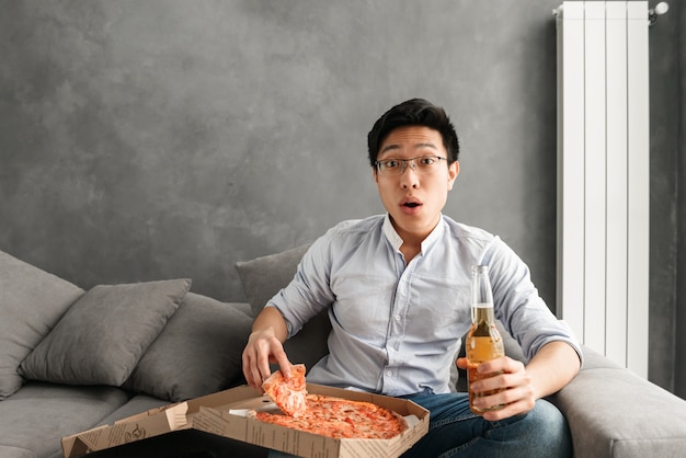 Portrait of a shocked young asian man eating pizza