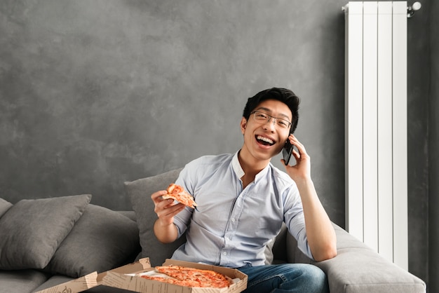 Portrait of a shocked young asian man eating pizza