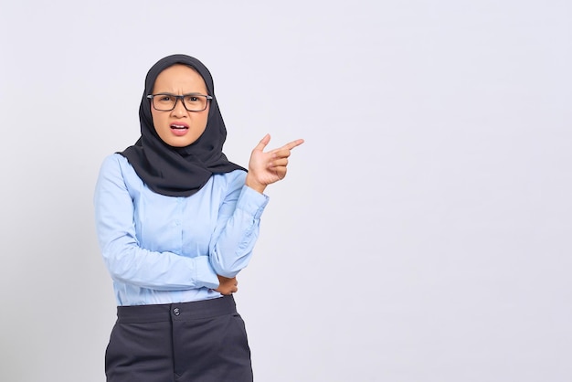 Portrait of shocked young Asian woman pointing finger at copy space isolated on white background