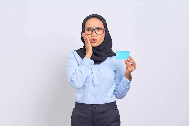 Portrait of shocked young Asian woman touching face cheek, holding credit card isolated on white background