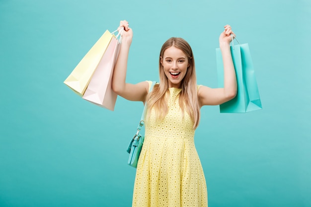 Portrait of shocked young attractive woman in yellow summer dress posing with shopping bag