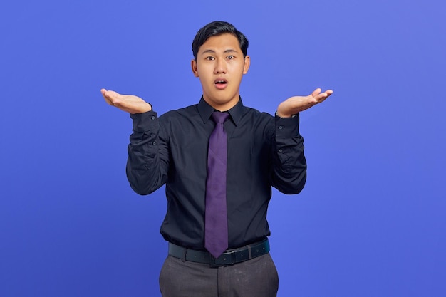 Portrait of shocked young handsome businessman showing copy space on palm on purple background