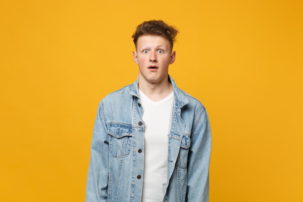 Portrait of shocked young man in denim casual clothes looking camera, keeping mouth open isolated on yellow orange background in studio. people sincere emotions, lifestyle concept. mock up copy space