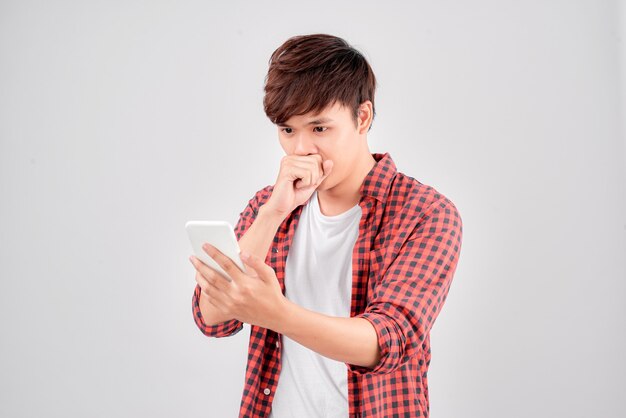 Portrait of a shocked young man looking at mobile phone isolated over white background, celebrating