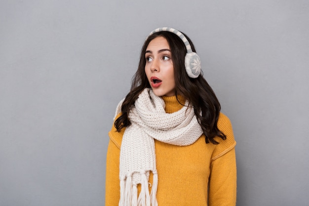 Portrait of a shocked young woman wearing sweater and scarf isolated over gray background