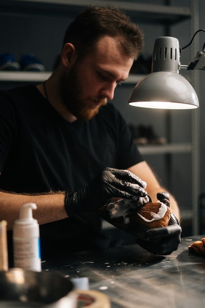 Portrait of shoemaker applying cleaning foam on old worn light brown leather shoes to be repaired