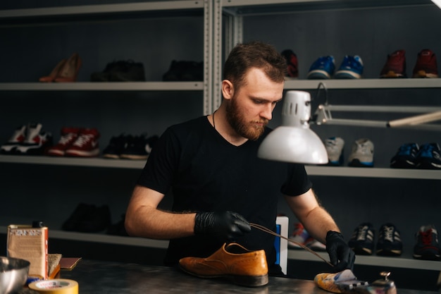 Portrait of shoemaker wearing black gloves inserts wooden shoe pad into worn light brown leather shoes