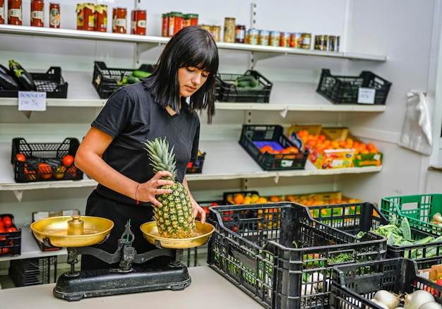 Portrait of shopkeeper in the greengrocer weighing a ripe pineapple