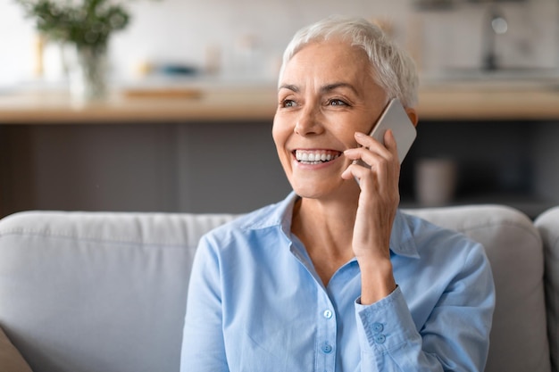 Portrait shot of happy mature lady talking on cellphone indoors