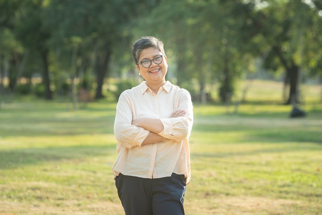 Portrait shot of happy, successful, relax caucasian senior asian woman smiling with glasses and carefree look toward the camera at the park as a background with copy space in natural autumn sunlight.