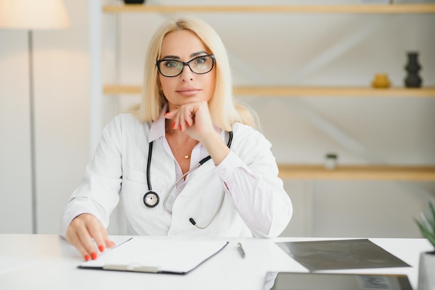 Portrait shot of middle aged female doctor sitting at desk and working in doctor office