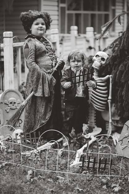 Photo portrait of siblings in costume standing by human skull during halloween celebration