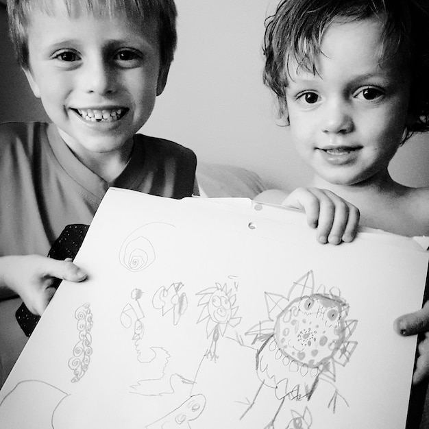 Photo portrait of siblings holding drawing at home