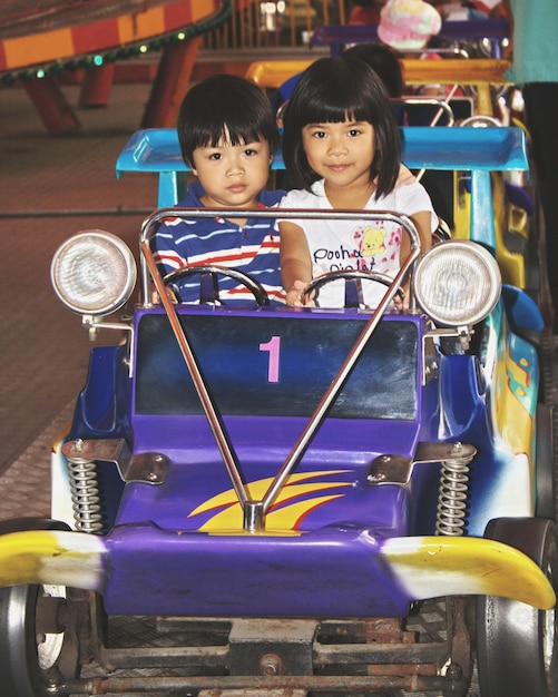 Photo portrait of siblings sitting in bumper car at amusement park