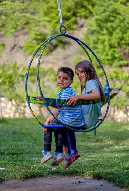 Photo portrait of siblings sitting on swing in park