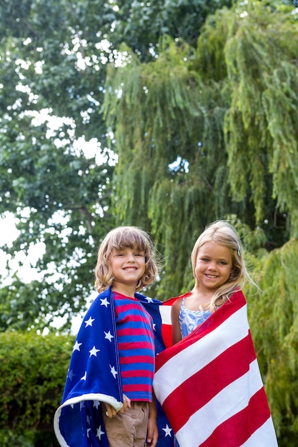 Portrait of siblings wrapped in American flag at back yard