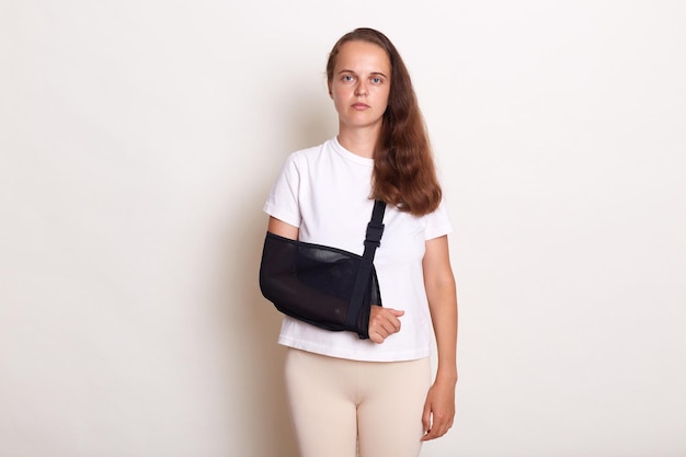 Portrait of sick arm broken caucasian woman with arm sling\
supported on her hand being injured by accident and healthcare\
posing isolated on white background