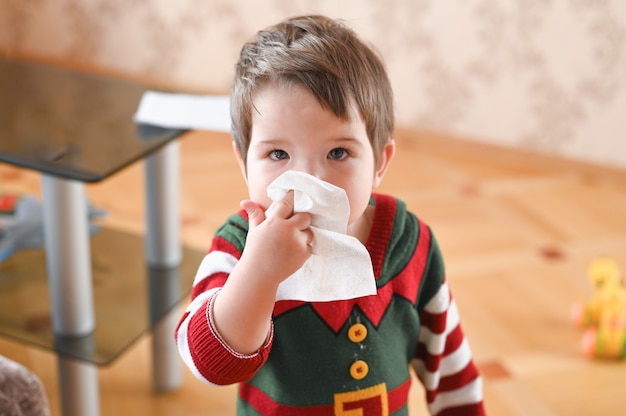 Portrait of a sick boy cleaning his nose with a napkin. Flu season concept