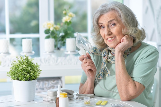 Portrait of sick senior woman sitting at kitchen with inhaler