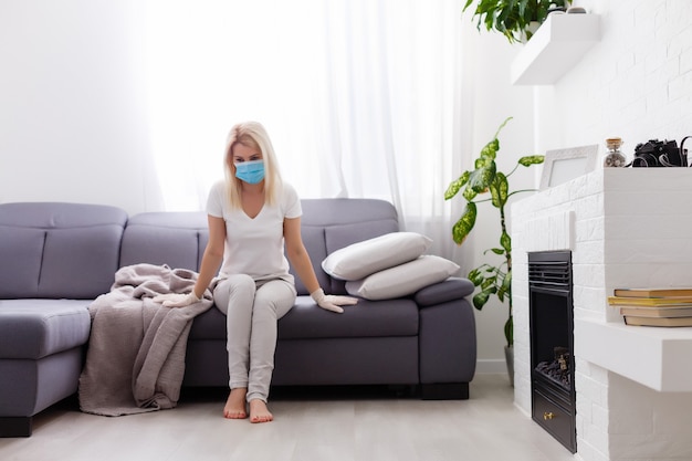 Portrait of a sick woman alone . An infectious agent protection gear including a mask. An sick older woman wearing protective masks to protect against virus. Coronavirus. Quarantine at home.