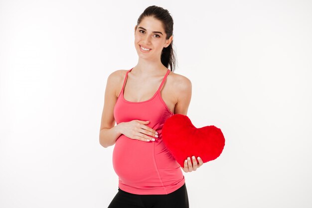 Portrait of a simling young pregnant woman holding pillow heart