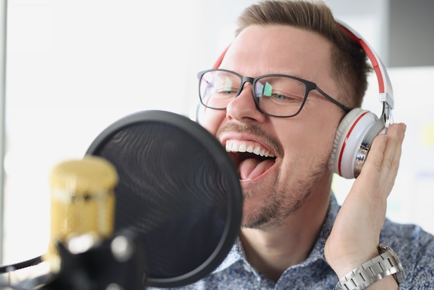 Portrait of singing young man in headphones front of microphone in studio work of presenter on