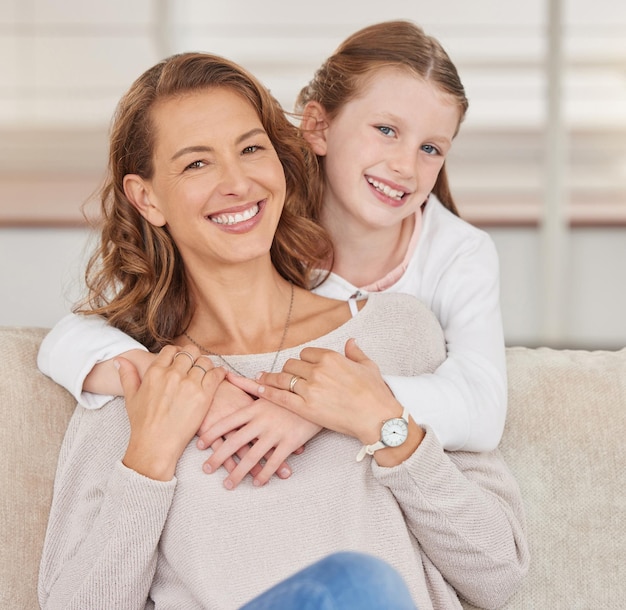 Portrait of a single mother and her daughter Adorable girl bonding with her single parent and hugging in the living room at home Smiling woman and her affectionate kid enjoying free weekend time