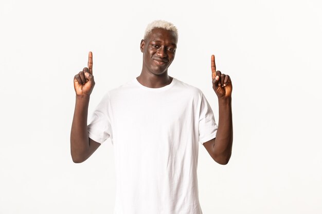 Портрет скептически настроенного белокурого афро-американского парня с ухмылкой и указательным пальцем вверх, показывая логотип