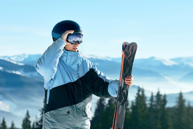 Portrait of a skier in the ski resort on the background of mountains and blue sky