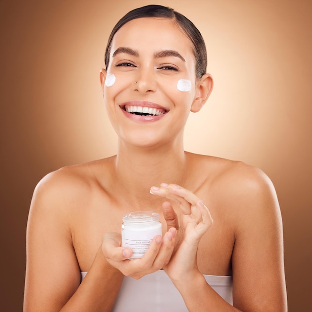 Portrait skincare and cream with a model woman in studio on a brown background for beauty or hydration Face beauty and product with a happy young female holding a container to apply moisturizer