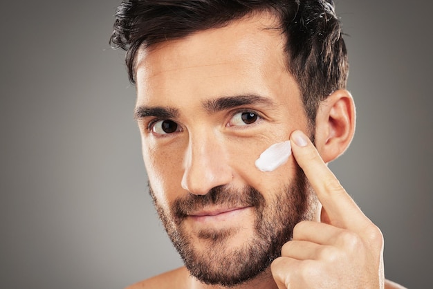 Portrait skincare and man with face cream in studio for moisturizing on gray background mockup Beauty male and model from Canada apply cosmetics product facial creme or lotion for healthy skin