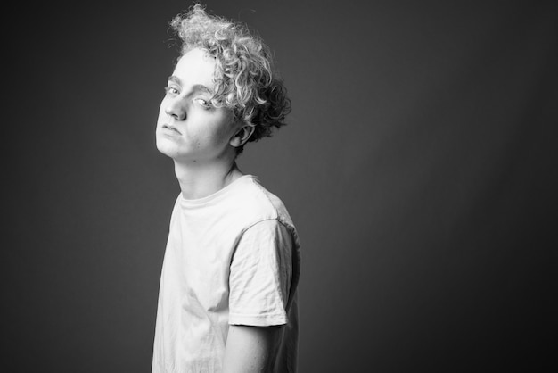 Portrait of skinny young man with curly hair on gray in black and white