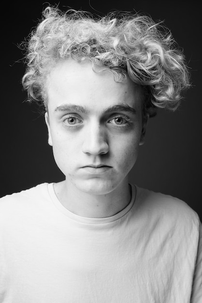 Portrait of skinny young man with curly hair on gray in black and white