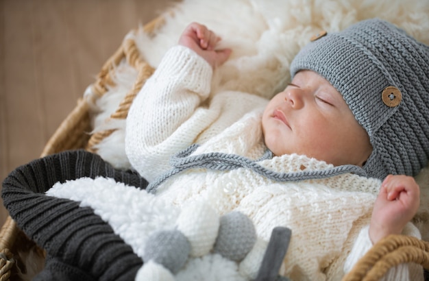 Portrait of a sleeping baby in a warm knitted hat with a knitted toy in the handle close up.