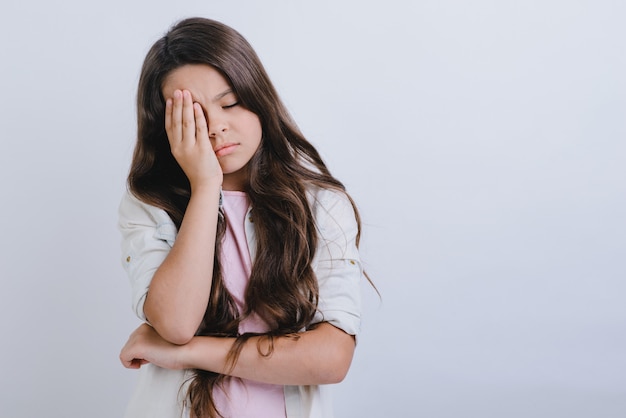 Portrait of a sleepy girl with long hair covering one eye with her hand.